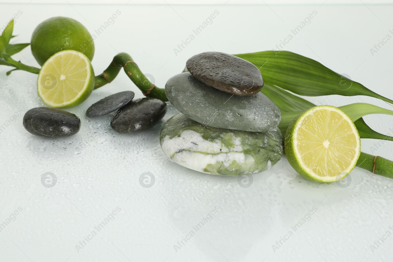 Spa composition with limes, massage stones and bamboo stem on wet surface Photo of Spa composition with limes, massage stones and bamboo stem on wet surface