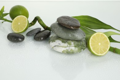 Photo of Spa composition with limes, massage stones and bamboo stem on wet surface