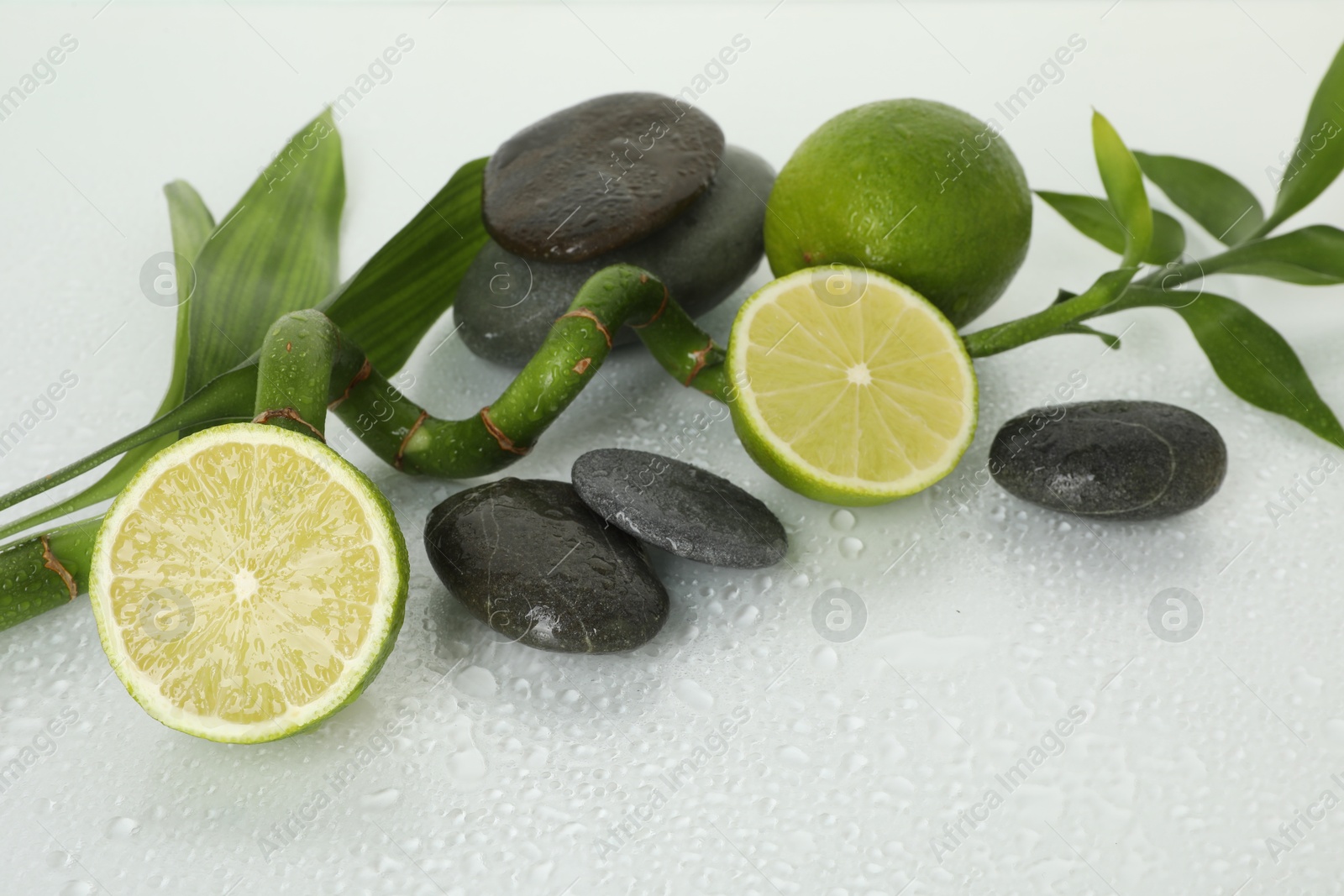 Spa composition with limes, massage stones and bamboo stem on wet surface Photo of Spa composition with limes, massage stones and bamboo stem on wet surface