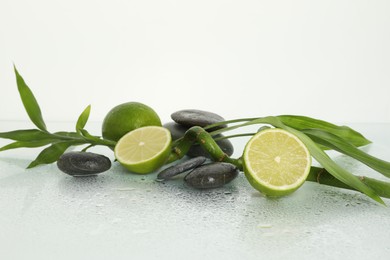Photo of Spa composition with limes, massage stones and bamboo stem on wet surface against white background
