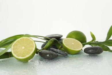 Photo of Spa composition with limes, massage stones and bamboo stem on wet surface against white background