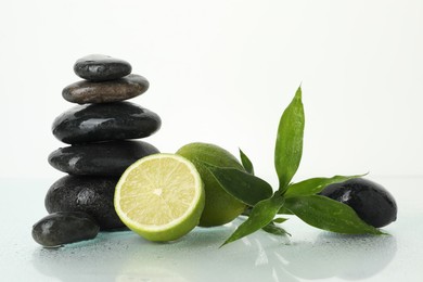 Photo of Spa composition with limes, massage stones and green leaves on wet surface against white background