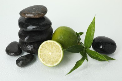 Photo of Spa composition with limes, massage stones and green leaves on wet surface against white background