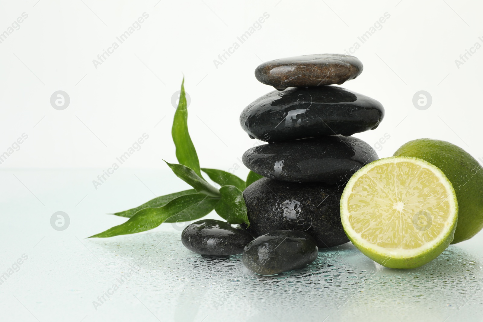 Spa composition with limes, massage stones and green leaves on wet surface against white background, space for text Photo of Spa composition with limes, massage stones and green leaves on wet surface against white background, space for text