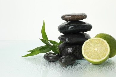 Photo of Spa composition with limes, massage stones and green leaves on wet surface against white background, space for text