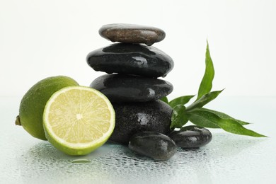 Photo of Spa composition with limes, massage stones and green leaves on wet surface against white background