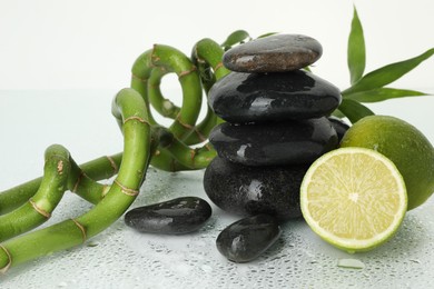 Photo of Spa composition with limes, massage stones and bamboo stems on wet surface against white background, closeup