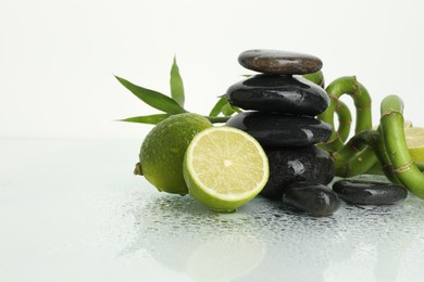 Photo of Spa composition with limes, massage stones and bamboo stems on wet surface against white background, space for text