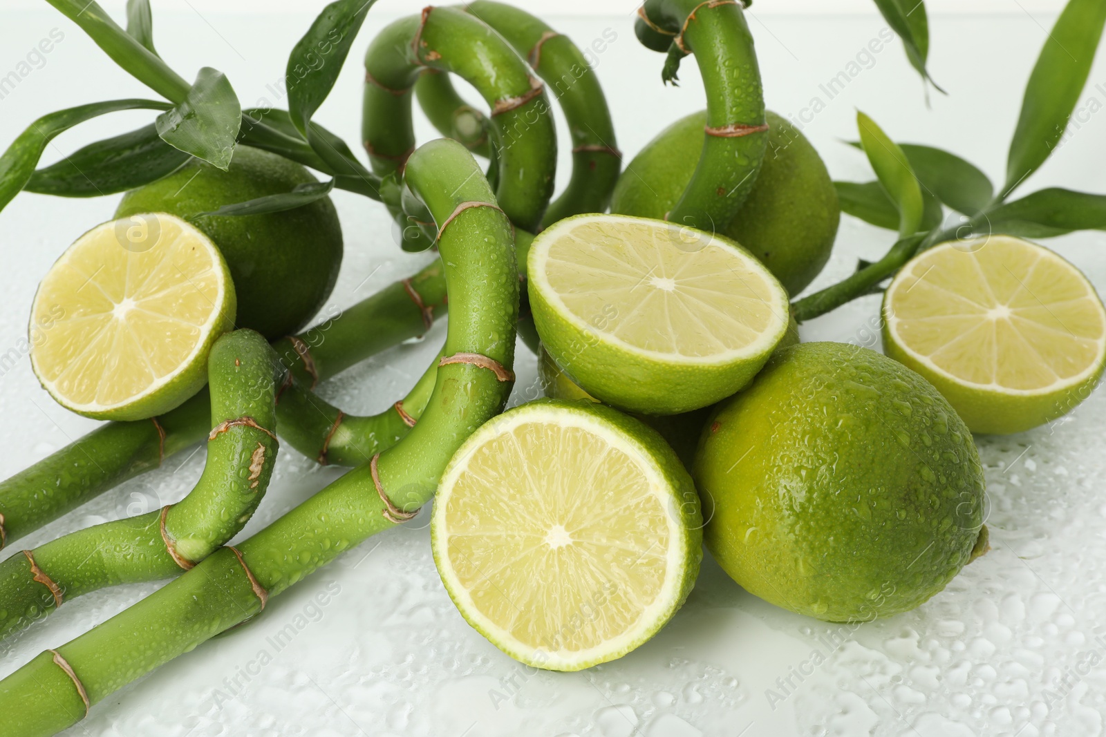 Photo of Fresh limes and bamboo stems on wet surface, closeup