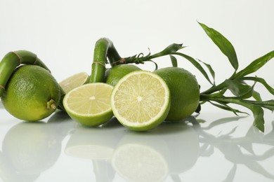 Photo of Fresh limes and bamboo stem on mirror surface against white background