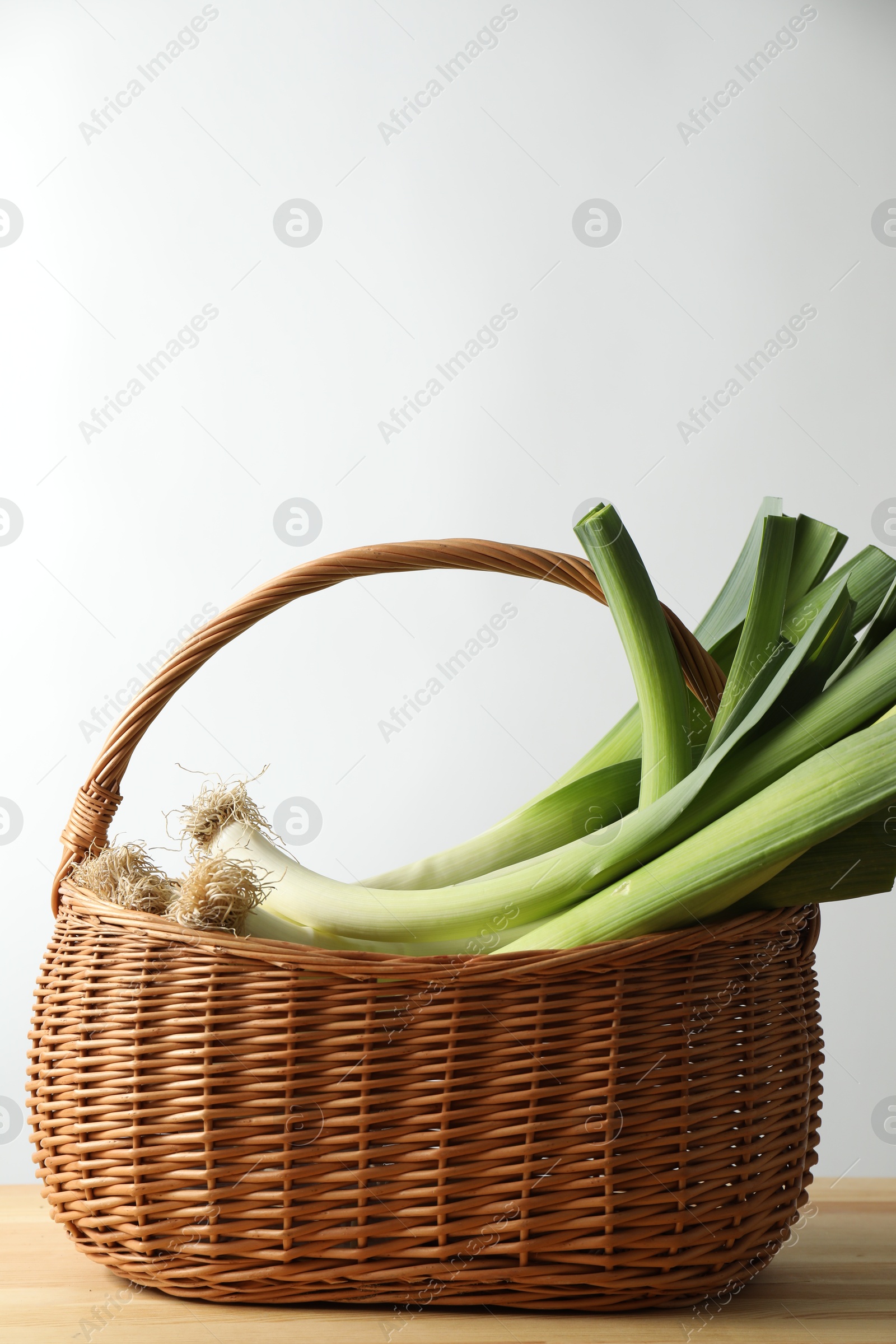 Photo of Fresh leeks in basket on wooden table