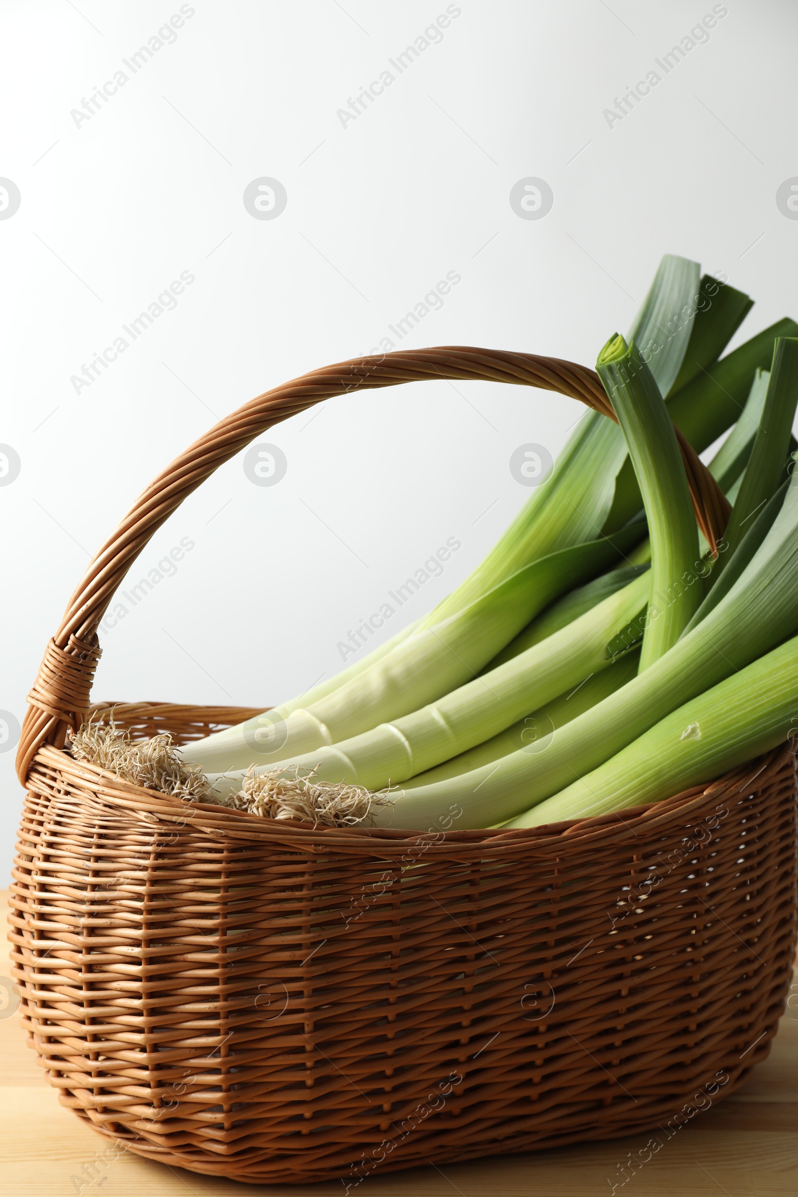 Photo of Fresh leeks in basket on wooden table