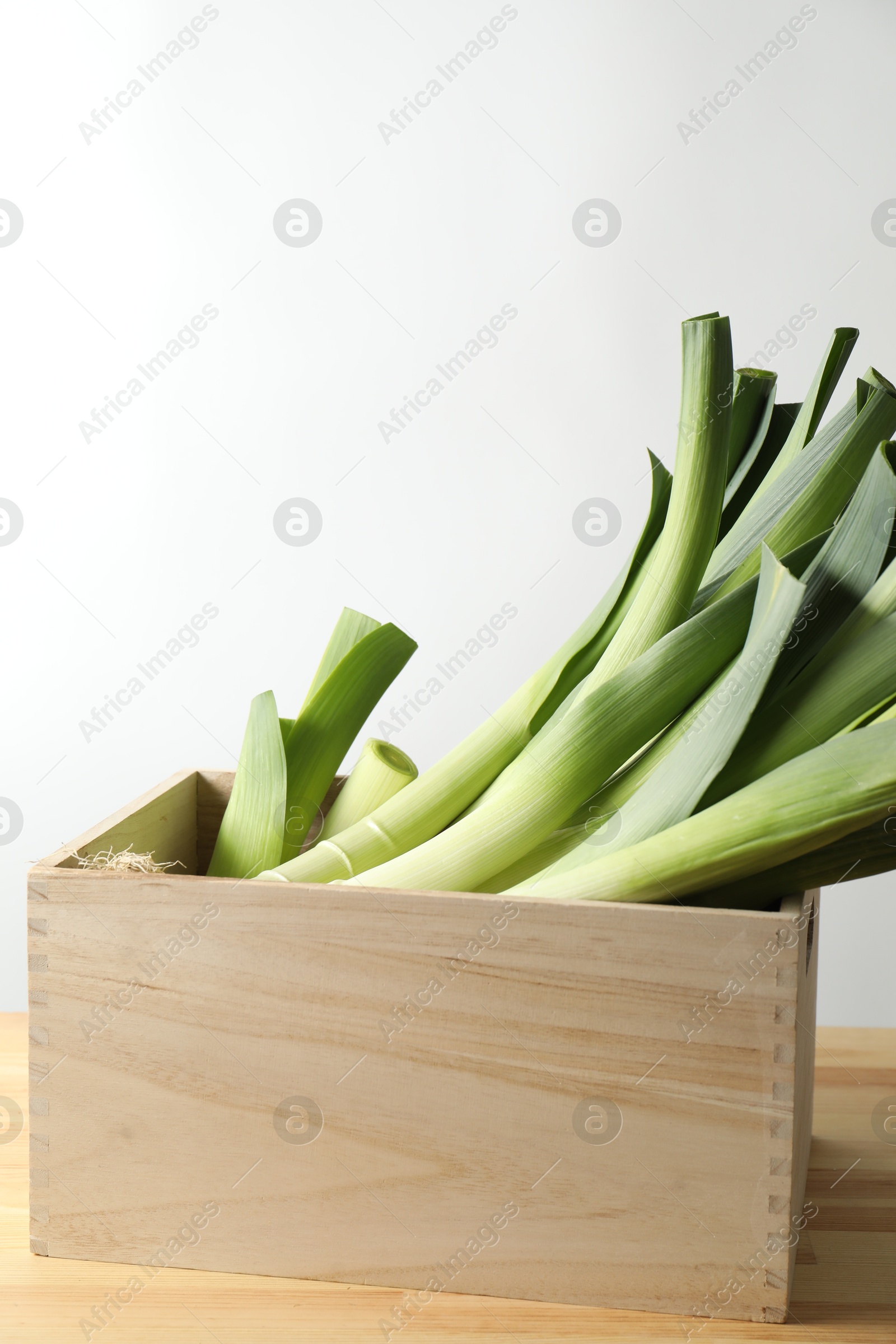 Photo of Fresh leeks in wooden crate on table. Space for text