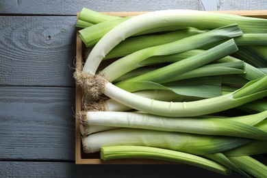 Photo of Fresh leeks in crate on grey wooden table, top view