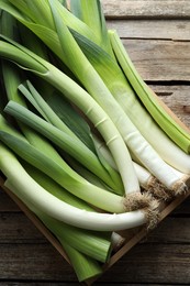 Photo of Fresh leeks in crate on wooden table, top view