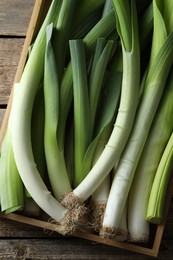 Photo of Fresh leeks in crate on wooden table, top view