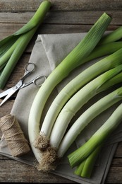 Photo of Whole fresh leeks, thread, scissors and towel on wooden table, flat lay