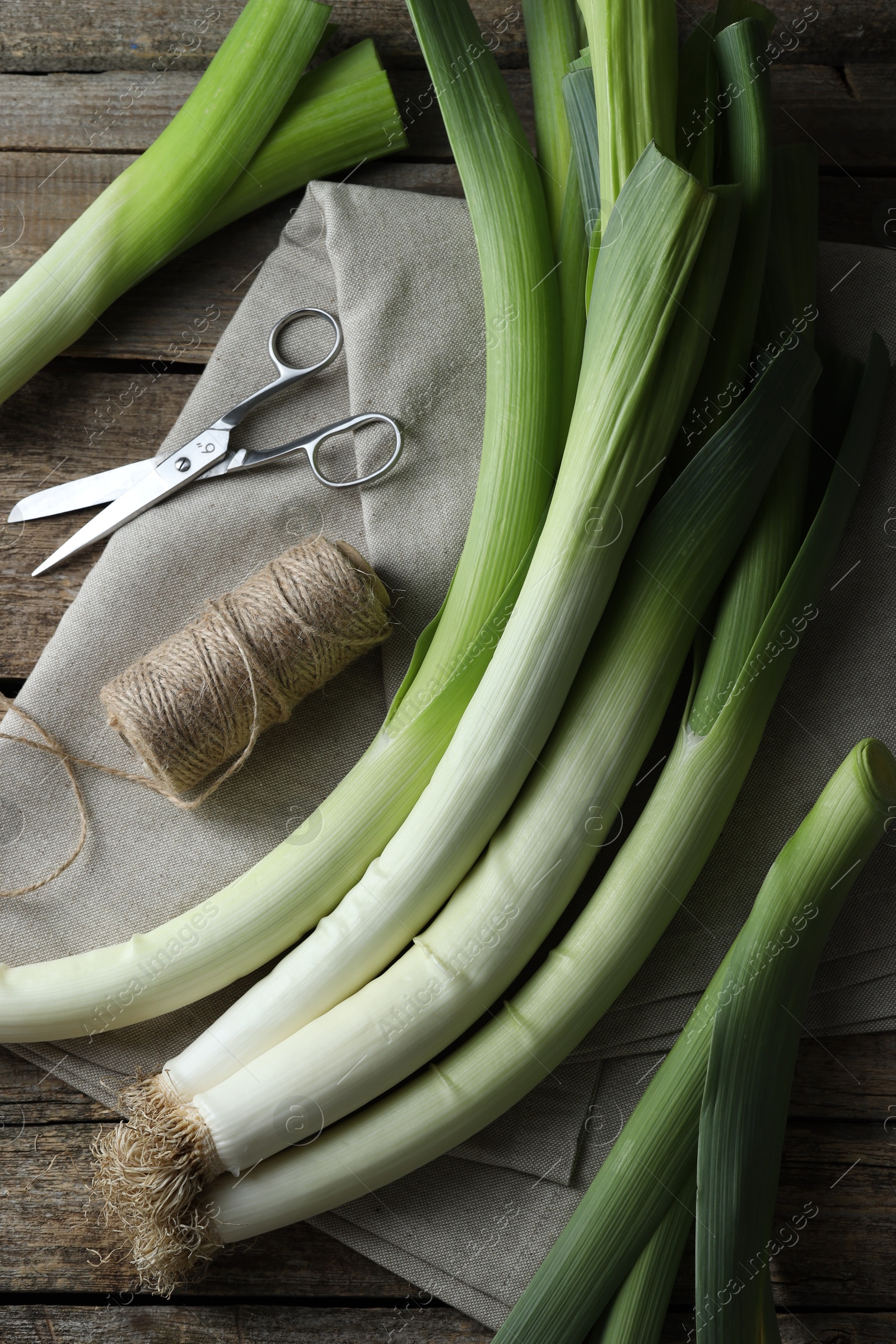 Photo of Whole fresh leeks, thread, scissors and towel on wooden table, flat lay