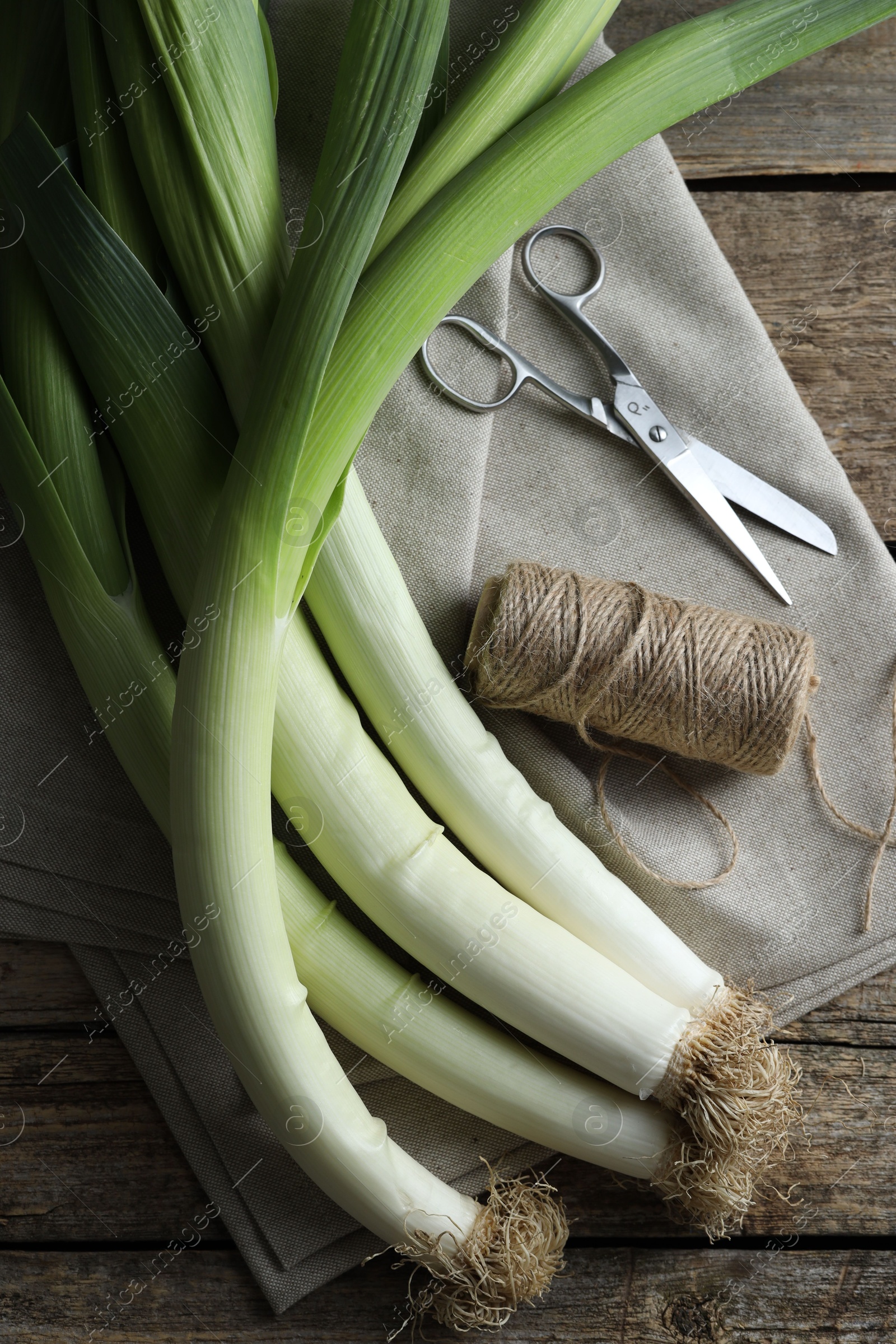 Photo of Whole fresh leeks, thread, scissors and towel on wooden table, flat lay