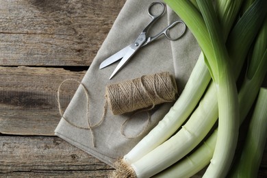 Photo of Whole fresh leeks, thread, scissors and towel on wooden table, flat lay. Space for text