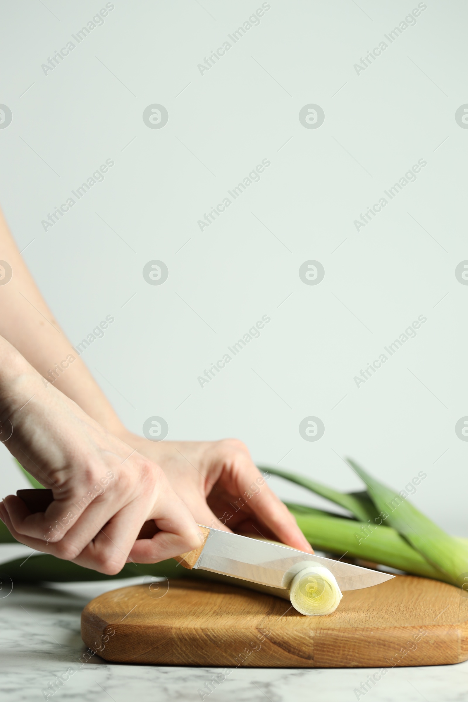 Photo of Woman cutting fresh leek at white table, closeup. Space for text