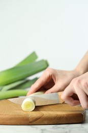 Photo of Woman cutting fresh leek at white table, closeup. Space for text