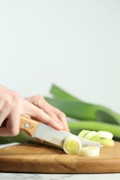 Photo of Woman cutting fresh leek at white table, closeup. Space for text