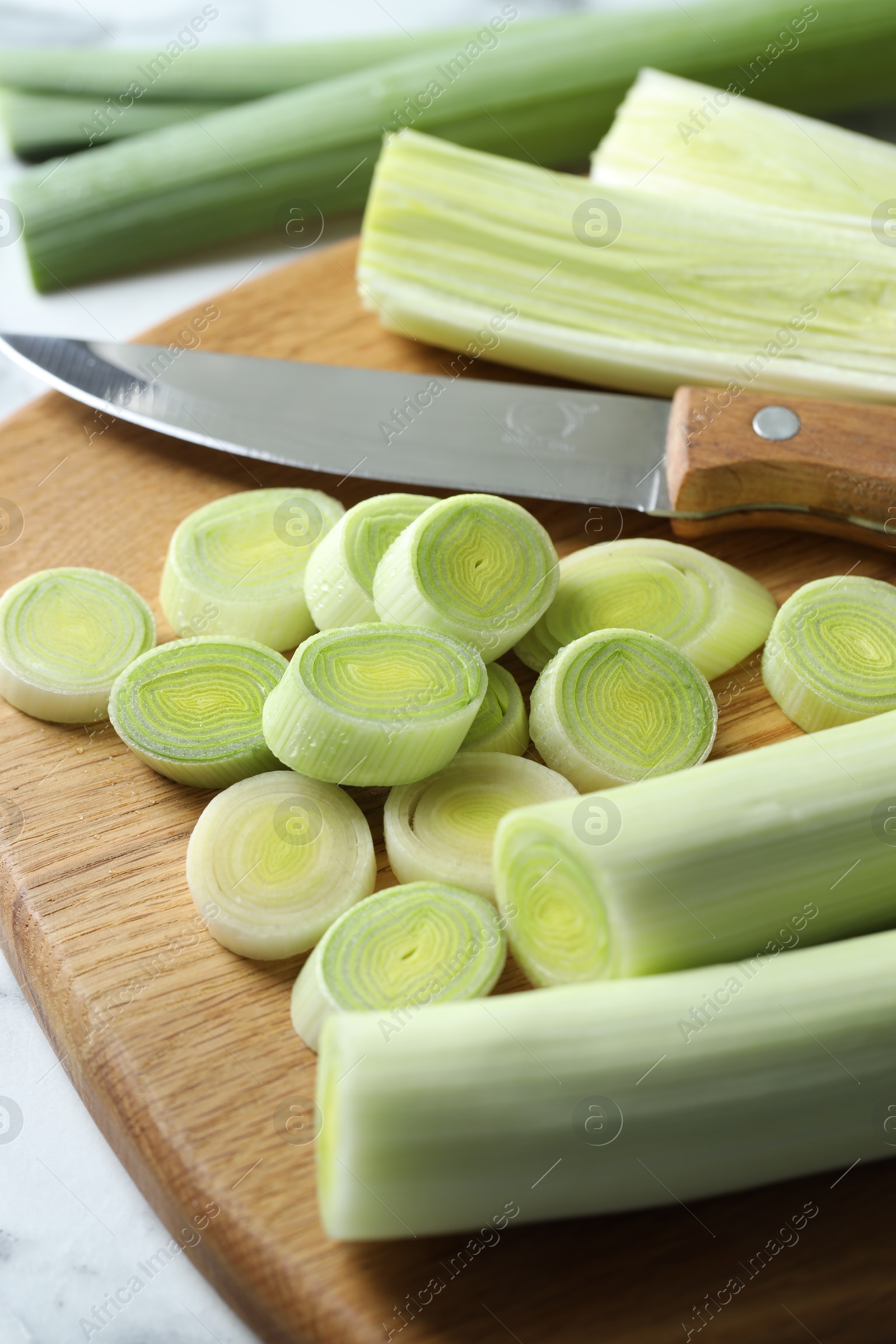 Photo of Chopped leeks, knife and board on white table, closeup