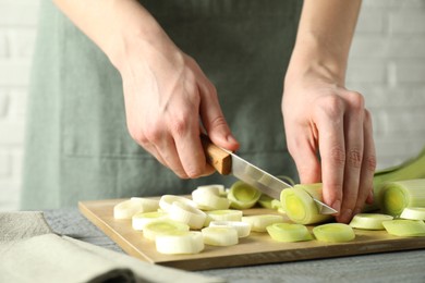 Photo of Woman cutting fresh leek at grey wooden table, closeup