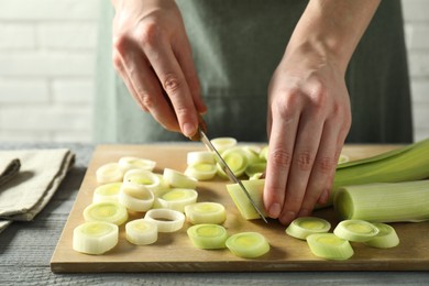 Photo of Woman cutting fresh leek at grey wooden table, closeup