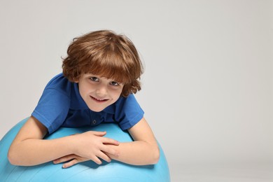 Little boy with fitness ball on light grey background, space for text