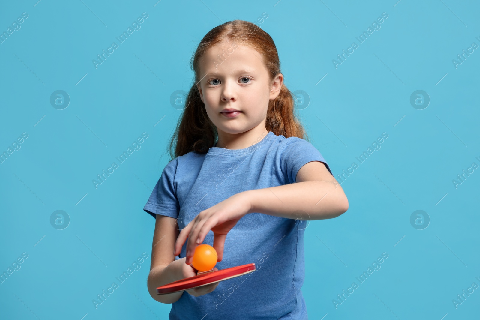 Photo of Little girl with ping pong racket and ball on light blue background