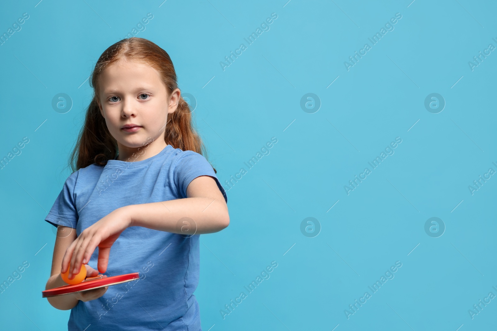 Photo of Little girl with ping pong racket and ball on light blue background, space for text