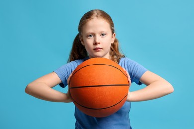 Photo of Little girl with basketball ball on light blue background