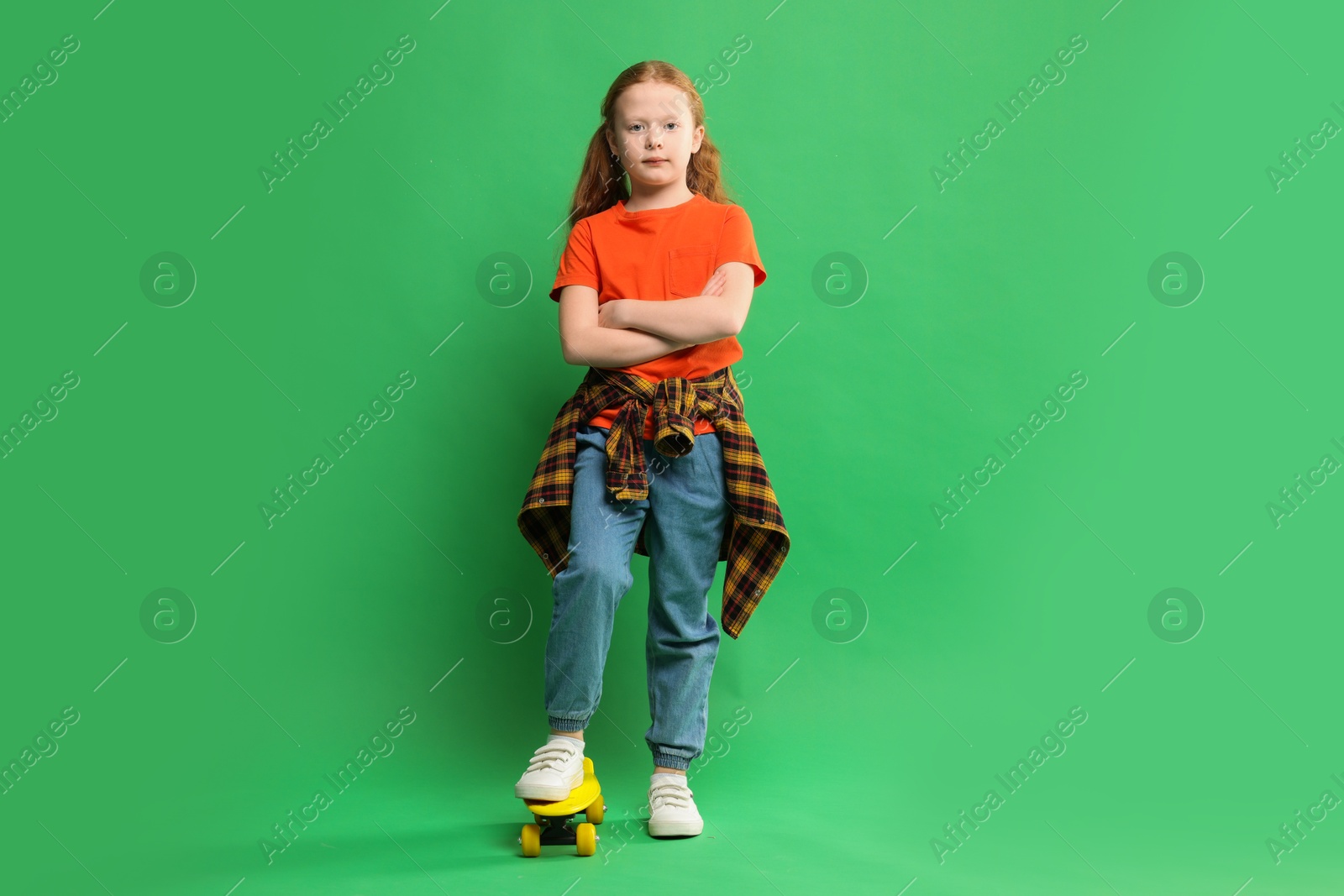 Photo of Stylish little girl with penny board on green background