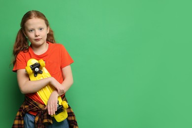 Photo of Stylish little girl with penny board on green background, space for text