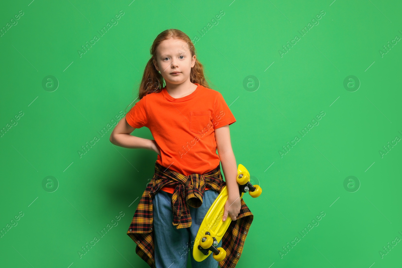 Photo of Stylish little girl with penny board on green background