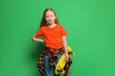 Stylish little girl with penny board on green background