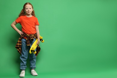 Photo of Stylish little girl with penny board on green background, space for text