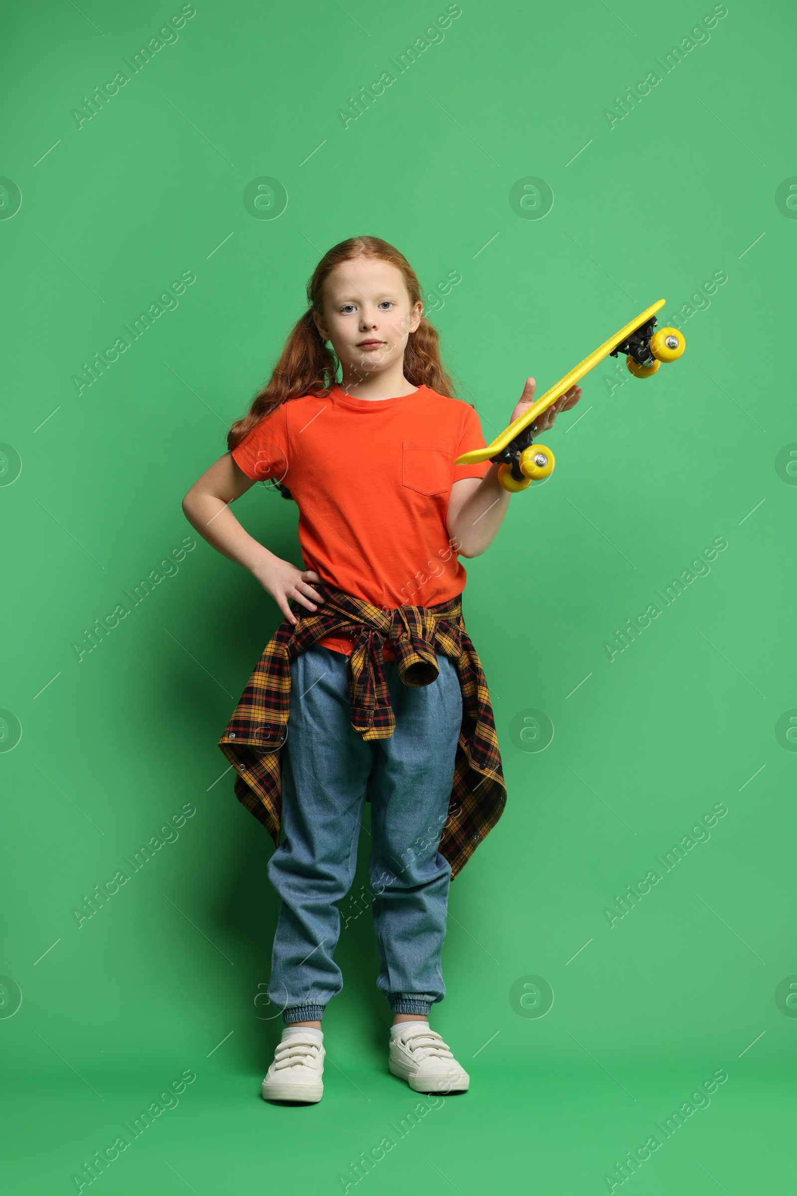 Photo of Stylish little girl with penny board on green background