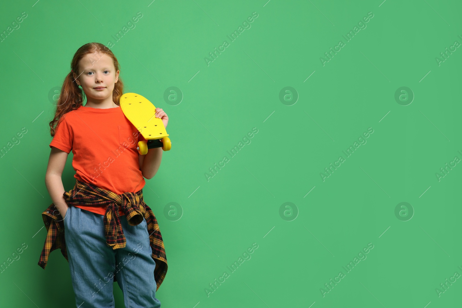 Photo of Stylish little girl with penny board on green background, space for text