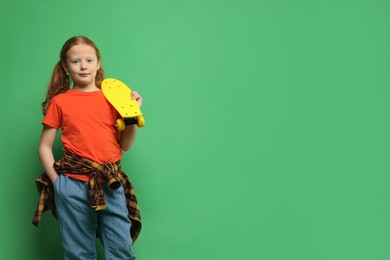 Photo of Stylish little girl with penny board on green background, space for text