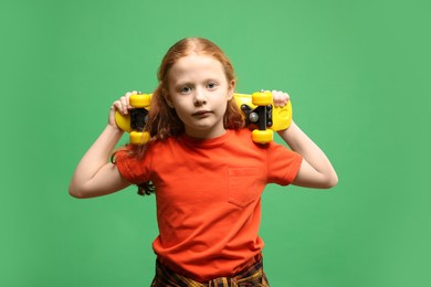 Photo of Stylish little girl with penny board on green background