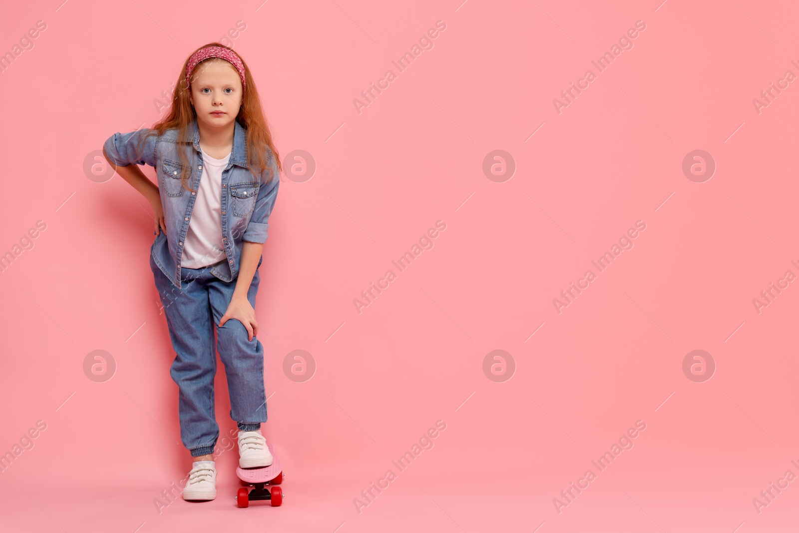 Photo of Little girl with penny board on pink background, space for text