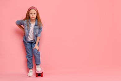 Little girl with penny board on pink background, space for text