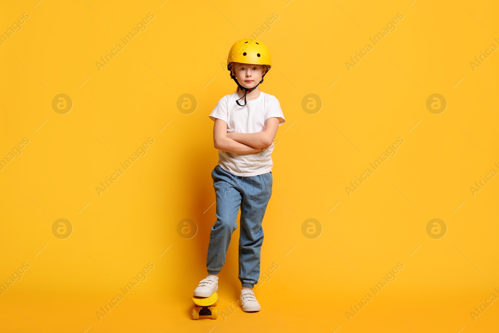 Photo of Little girl in helmet with penny board on orange background