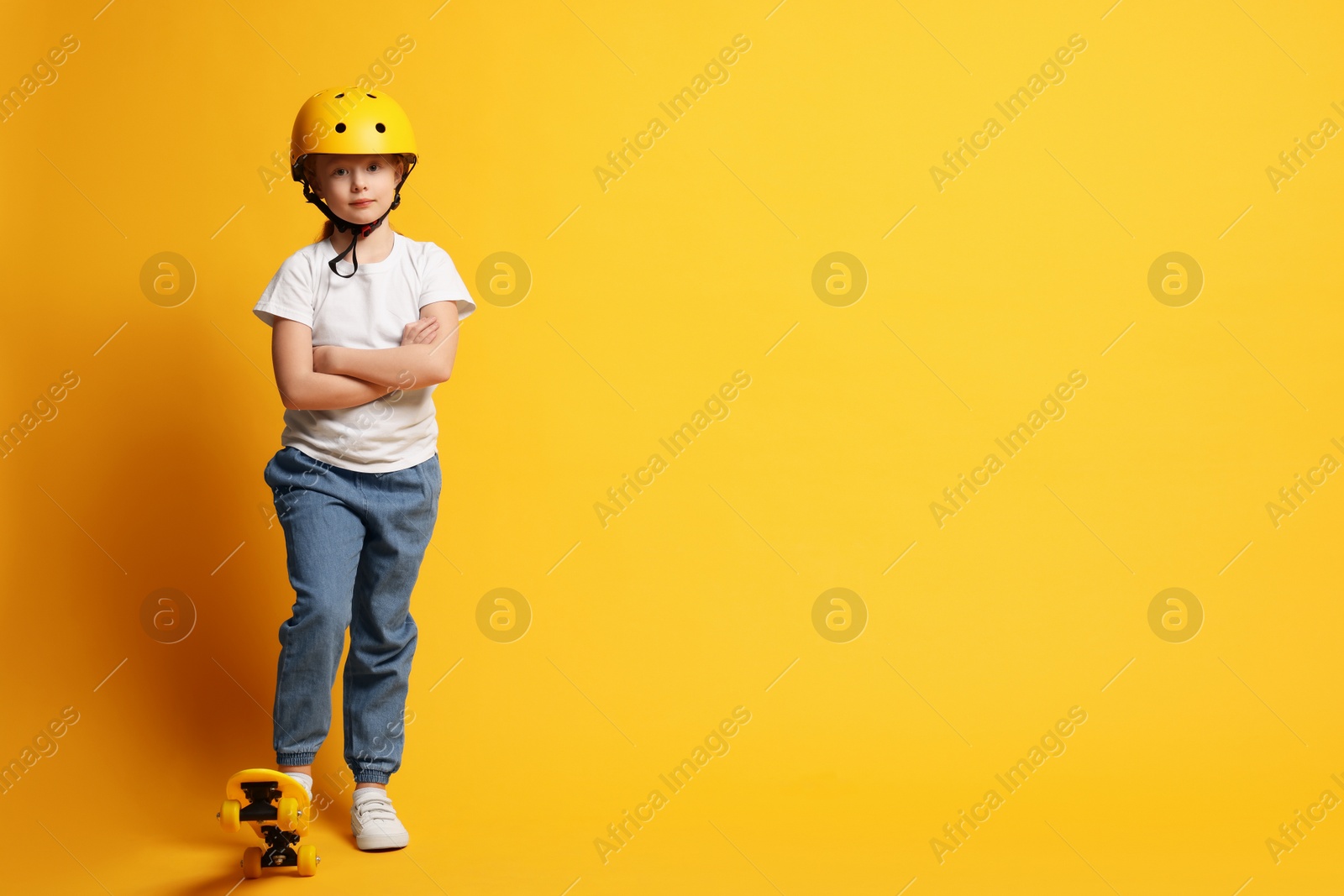 Photo of Little girl in helmet with penny board on orange background, space for text