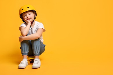 Photo of Little girl in helmet sitting on penny board against orange background, space for text