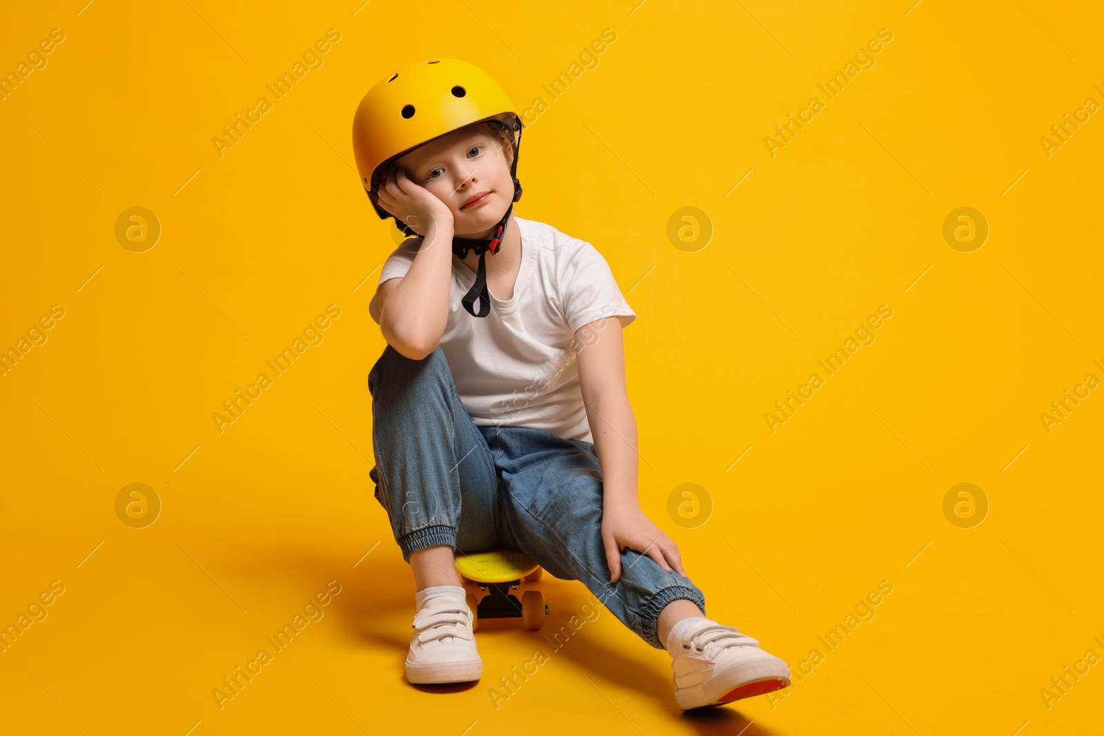 Photo of Little girl in helmet sitting on penny board against orange background