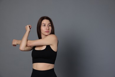 Woman in sportswear exercising on grey background, space for text